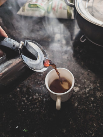 Pouring a hot shot of morning South Indian filter coffee from a moka pot in an Indian household. A...