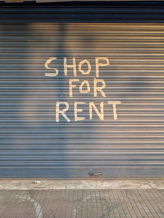 A closed shop with a blue metal shutter featuring the words 'Shop For Rent' painted in white.