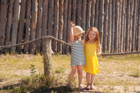 Two little girls standing at the fence ,chatting,laughing and dancing barefootの写真素材