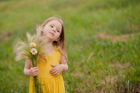 girl with a bouquet of wheat and flowers on the background of green grassの写真素材