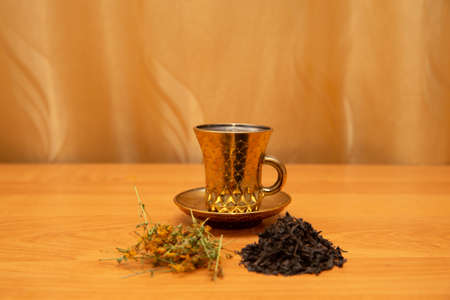 Golden cup with tea and hypericum. On the golden background, orange table. Golden curtain. St Johns...