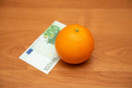 Orange and 100 euro. The table is orange. Pay for food, fruit. It contains a lot of vitamin C. The focus is on the orange.の写真素材