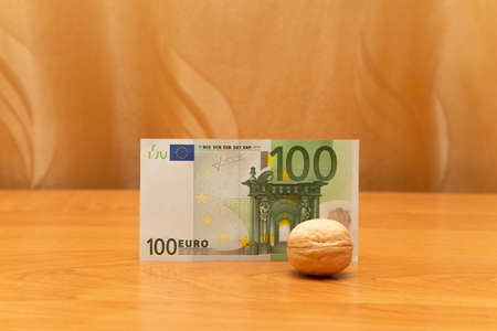 Walnut is in front of 100 euro. The table is orange. The curtains are golden. Buy nuts. There is space around. The focus is on the moneyの写真素材