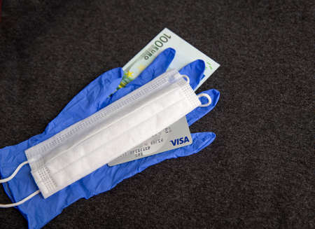 Mari El, Russia - May 10, 2021: Credit visa card, blue latex glove and white mask. Dark textile background. 100 eurosのeditorial素材