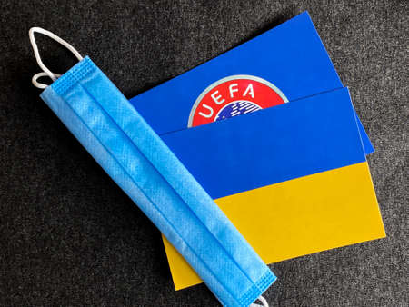 Mari El, Russia - June 12, 2021: UEFA logo and Ukraine, Ukrainian flag is near a blue mask on the dark gray background. Tourist trip. European Football Championship, Euroのeditorial素材