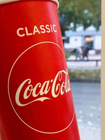 Mari El, Russia - September 19, 2021: Coca-cola red paper glass is on a light table. The street is on the background, a view from the window. Selective focusのeditorial素材