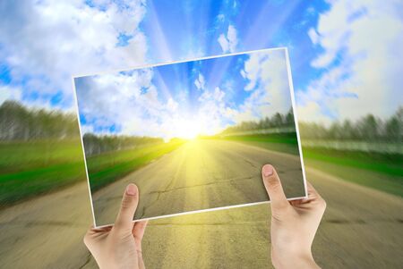 Hand holding photo of road background with sunriseの写真素材