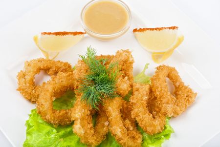 Deep-fried squid with salad leaves, sauce, green and lemon on a white backgroundの写真素材