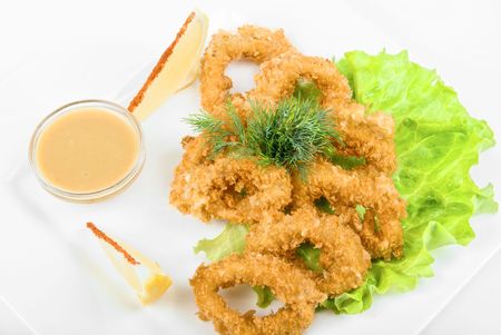 Deep-fried squid with salad leaves, sauce, green and lemon on a white backgroundの写真素材