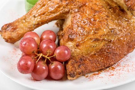 Half roasted chicken closeup with grape on a whiteの写真素材