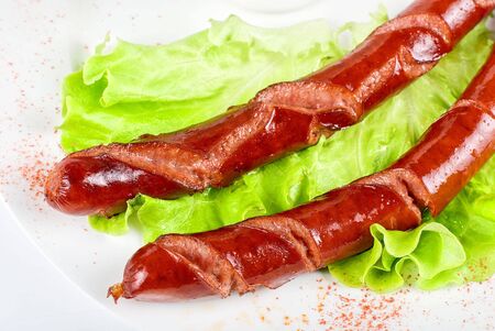 grilled sausage closeup with lettuce and sauce isolated on whiteの写真素材