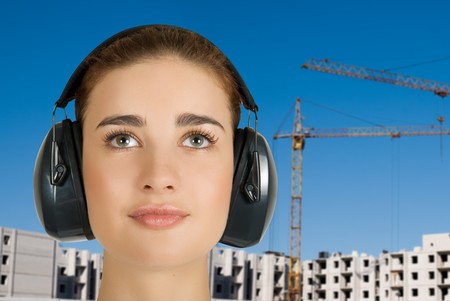 Builder pretty girl at safety earphone on a building backgroundの写真素材