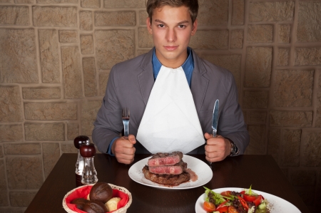 man holding a knife and a fork ready to eat a beef steakの写真素材