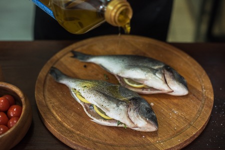 Fresh uncooked dorado with lemon, herbs, oil and spices ready for preparingの写真素材