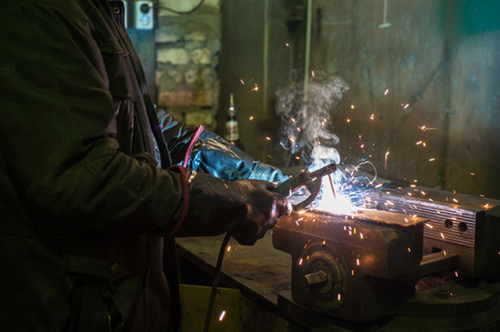 worker welding metal with sparks at factory