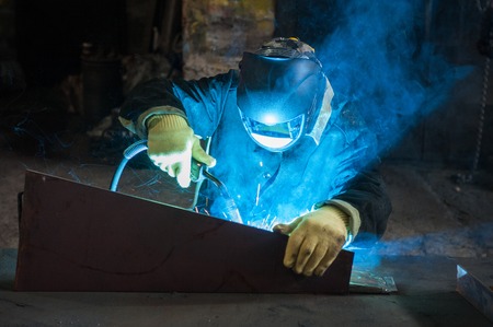 worker welding metal with sparks at factory