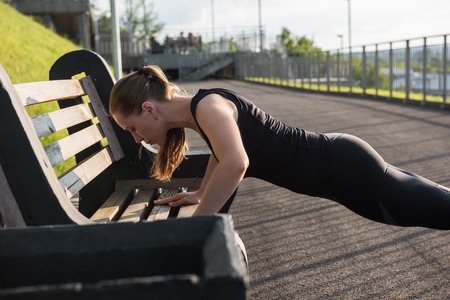 A woman in sportswear doing push ups in the city park in sunny evening.の写真素材