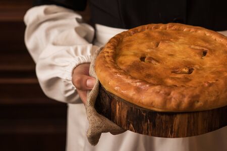 Pie from potato meat cheese and vegetables. Freshly baked pie in hands of woman in uniformの写真素材