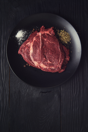 Fresh raw beef meat steaks in the black plate with spices on black wooden backgroundの写真素材