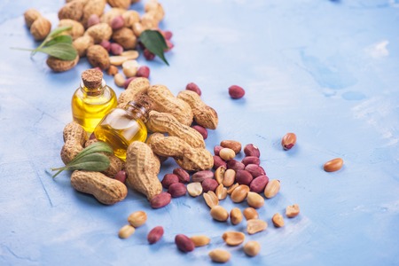 Natural peanuts with oil in a glass jar on the blue concrete background