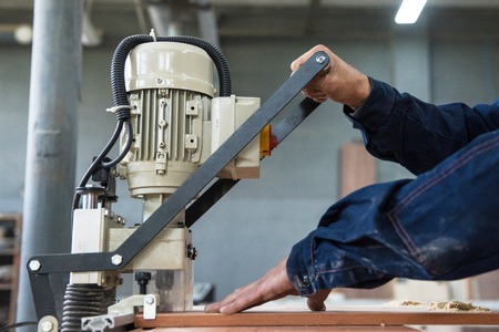 Furniture production concept: man working at machine and making furniture part