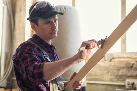 The worker makes measurements of a wooden board with corner ruler.の写真素材