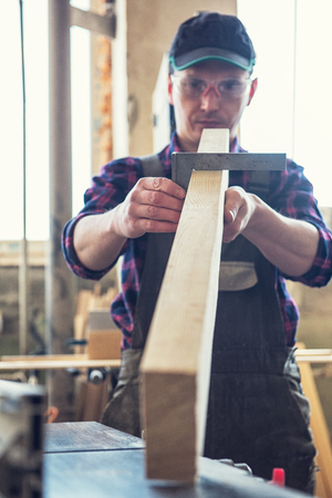 The worker makes measurements of a wooden board with corner ruler.の写真素材