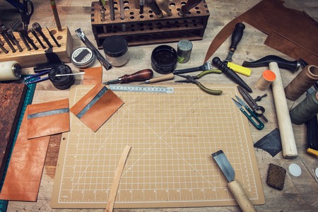 Leathermakers work desk. Tools and leather at cobbler workplace. Tools for craft production of leather goods on wooden table.の写真素材