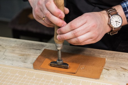 Man makes a stamp on the leather textile at a workshop. Concept of handmade craft production of...