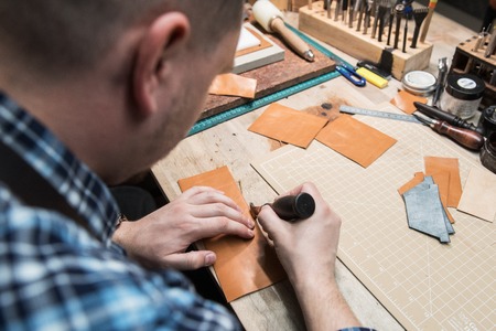 Man working with leather textile at a workshop. Concept of handmade craft production of leather goods.の写真素材