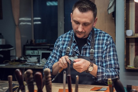 Man working with leather textile at a workshop. Concept of handmade craft production of leather goods.の写真素材