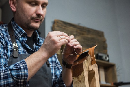 Man sewing leather wallet at a workshop. Concept of handmade craft production of leather goods.