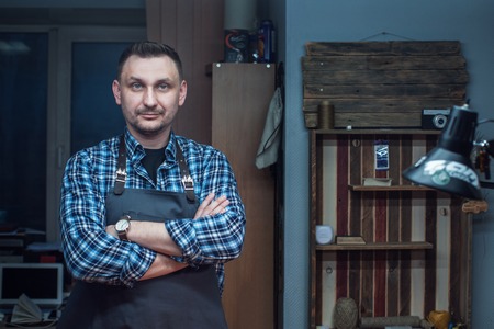 Man working with leather textile at a workshop. Male portrait. Concept of handmade craft production of leather goods.の写真素材