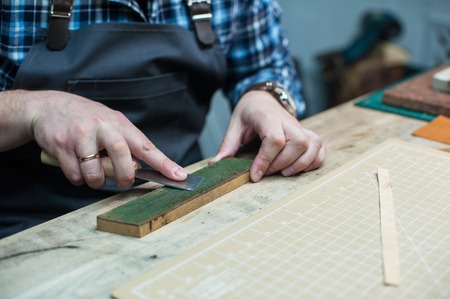 Man making leather wallet at a workshop. Concept of handmade craft production of leather goods.