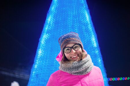 Outdoor photo of beauty happy smiling woman posing on festive fir-tree background. New Year...