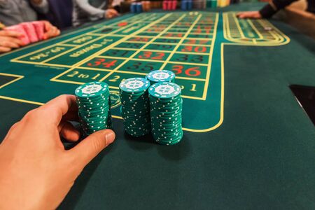 Casino, gambling and entertainment concept - male hand with stack of poker chips on a green table backgroundの写真素材
