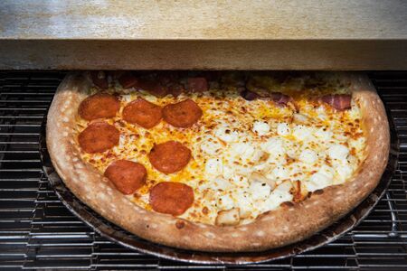 Preparing pizza in oven at restaurant kitchen, ready pizza from electric conveyor ovenの写真素材