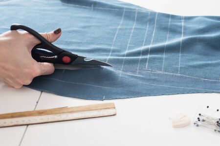 Woman dressmaker cutting fabric textile with scissors