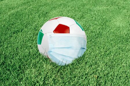 Soccer ball in italian colors with mask on green field. Virus threatened championship conceptの写真素材