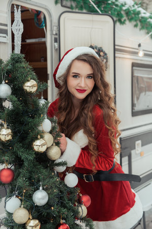 Young woman in santa costume decorates the Christmas tree at winter campsiteの写真素材
