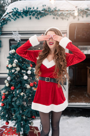 Young woman in santa costume decorates the Christmas tree at winter campsiteの写真素材