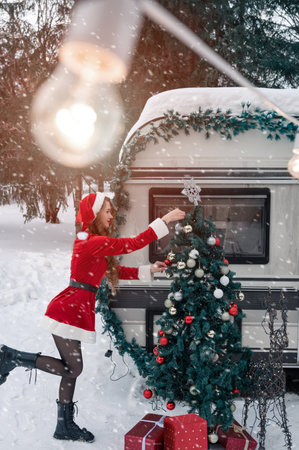 Young woman in santa costume decorates the Christmas tree at winter campsiteの写真素材
