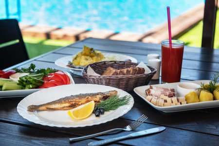 Fried grayling fish on a plate with any appetizers on swimming pool background. Resting and relaxing concept.の写真素材