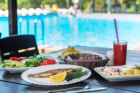 Fried grayling fish on a plate with any appetizers on swimming pool background. Resting and relaxing concept.の写真素材