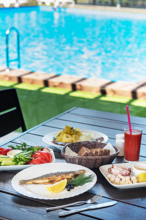 Fried grayling fish on a plate with any appetizers on swimming pool background. Resting and relaxing concept.の写真素材