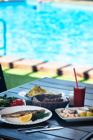Fried grayling fish on a plate with any appetizers on swimming pool background. Resting and relaxing concept.の写真素材