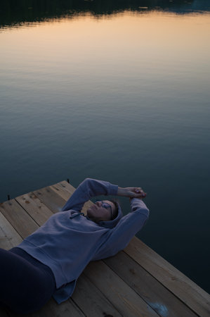 Woman lying down on the pier at lake, closeup portrait, summer sunsetの写真素材
