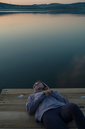 Woman lying down on the pier at lake, closeup portrait, summer sunsetの写真素材