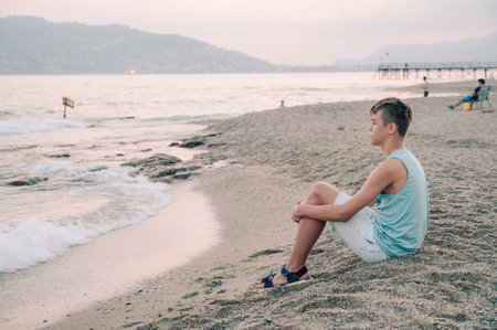 Boy teen sits on the beach and looks at the sea in Alanya city, Turkey. Traveling or vacation conceptの写真素材