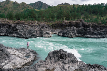 A solitary figure stands firmly on the rocks by a flowing, turquoise Katun river that is surrounded by lush greeneryの写真素材